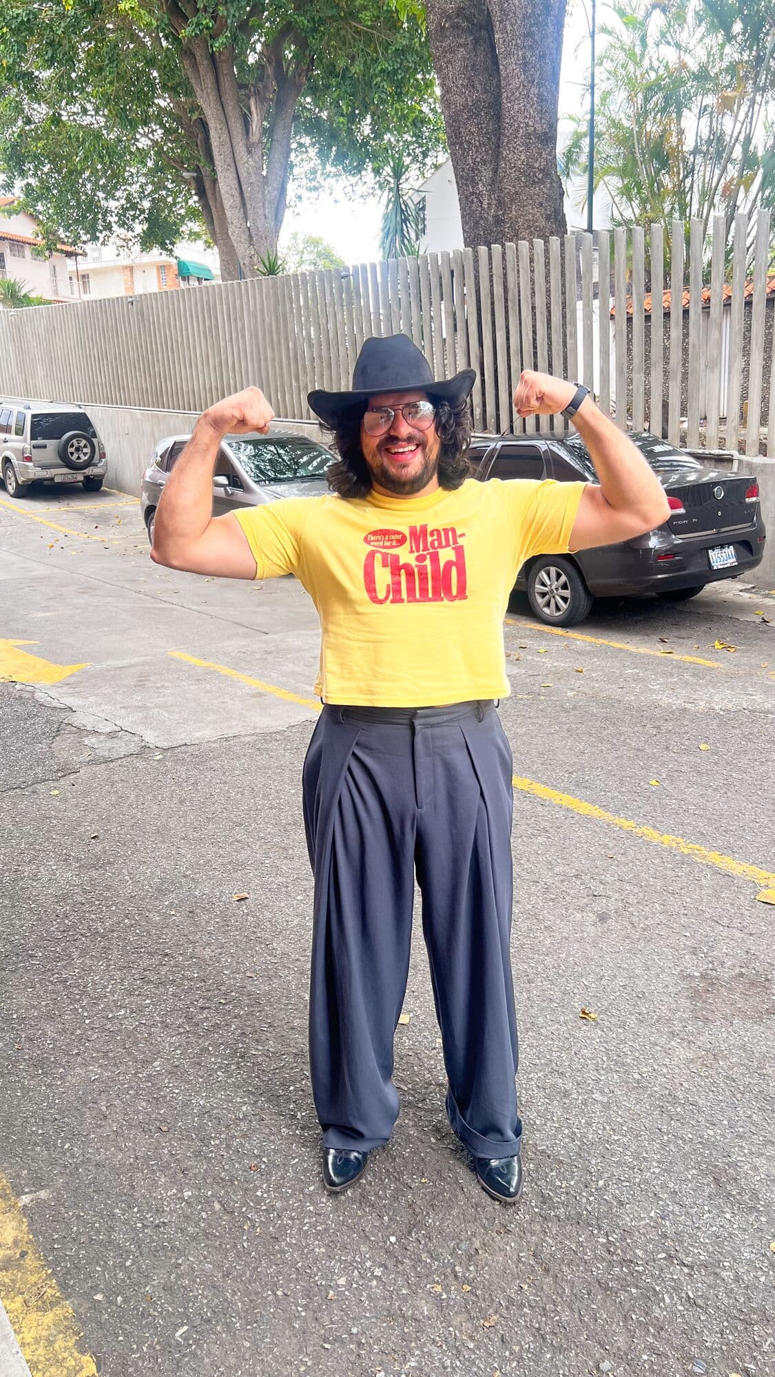 Yisus con sombrero y camiseta amarilla, flexionando los brazos en plena calle